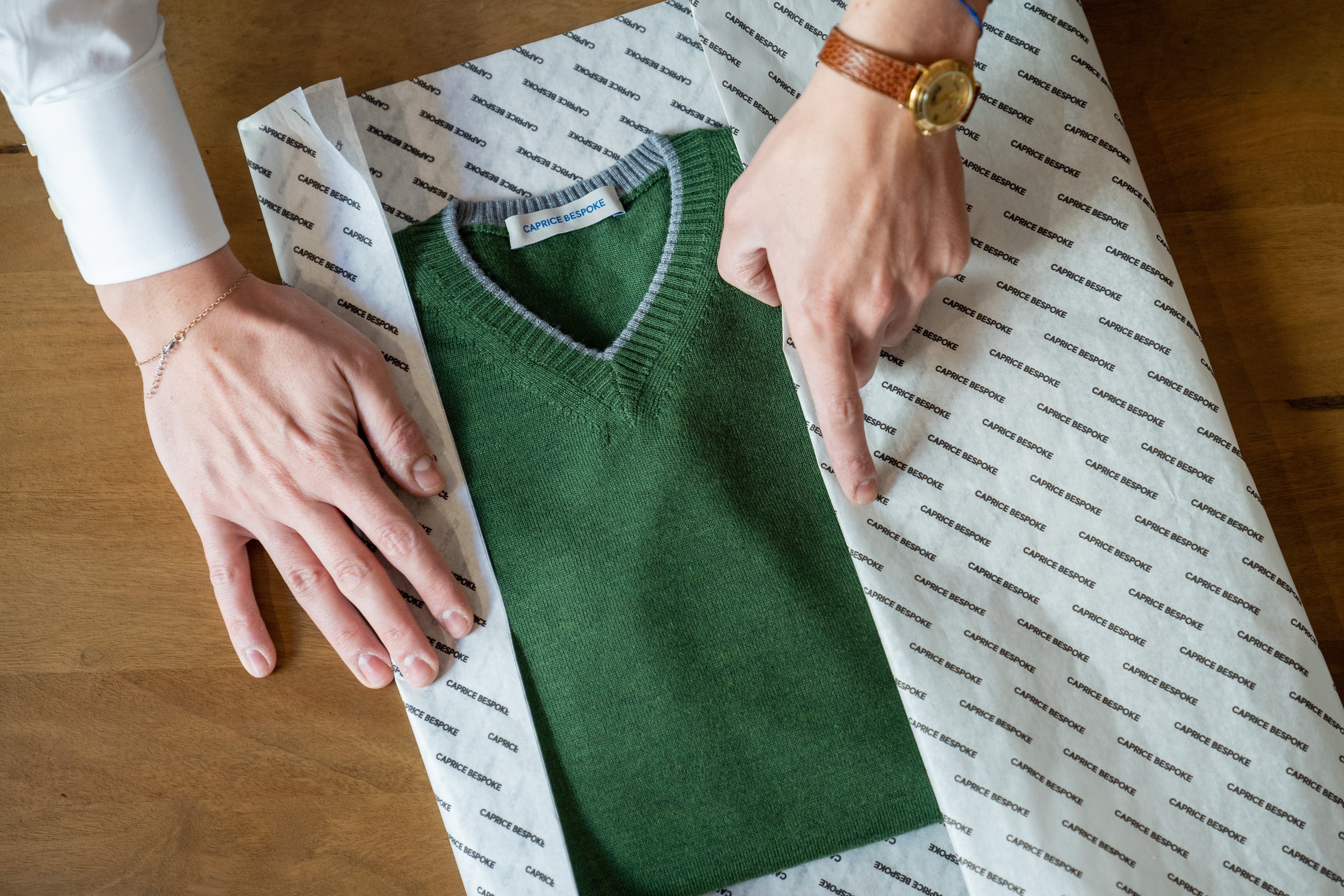 luxury-green-v-neck-sweater-folded-in-branded-caprice-bespoke-tissue-paper-on-wooden-table