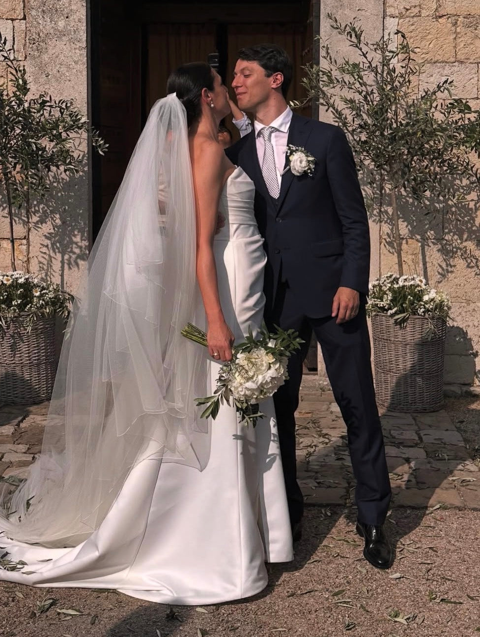 wedding-couple-standing-close-together-outdoors-with-flowers-and-a-stone building-in-the-background